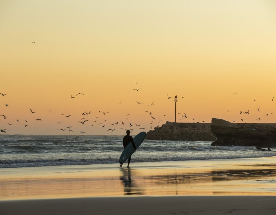 Jeune homme avec une planche de surf pendant un coucher de soleil 1280x853 1